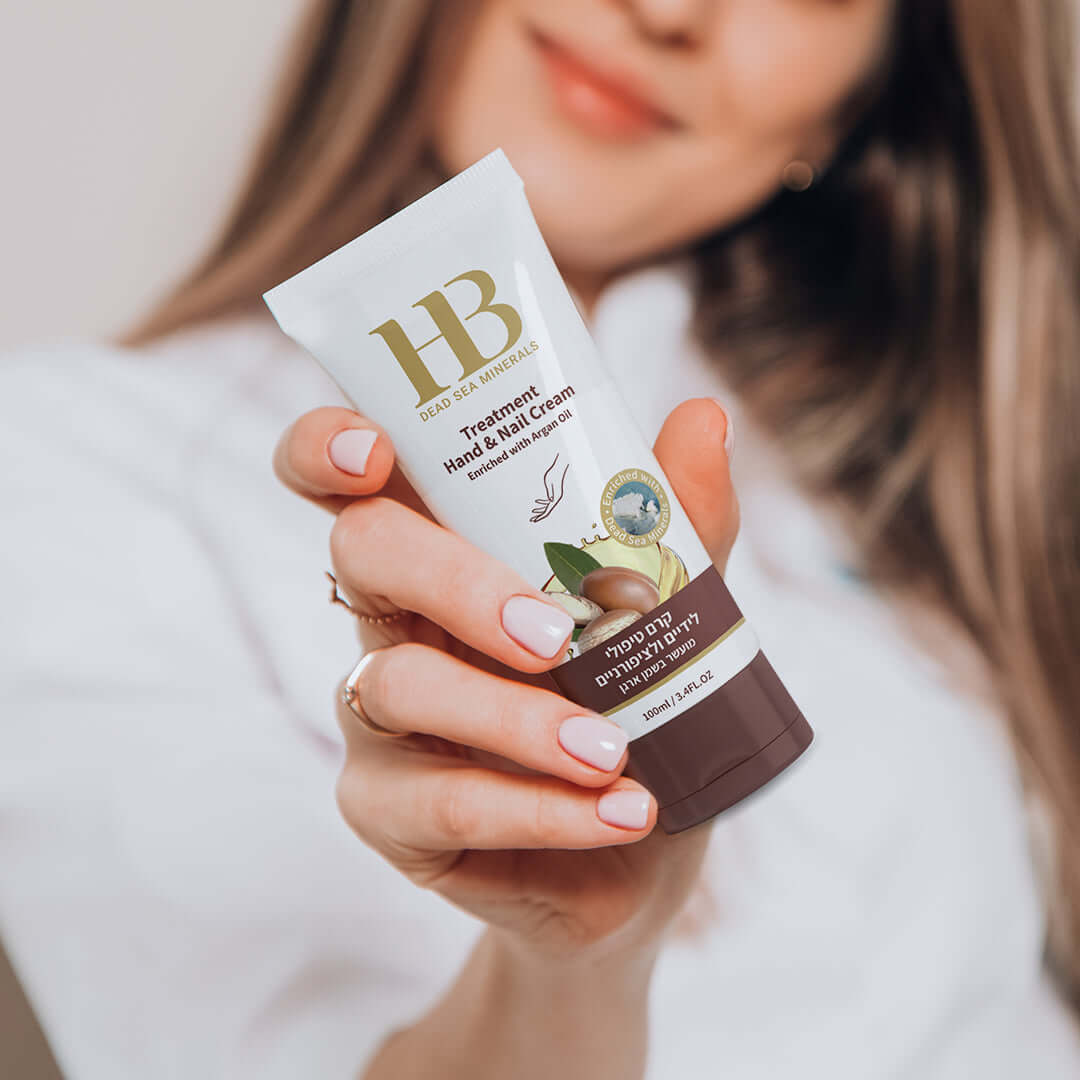 Hand holding a tube of HB Hand & Nail Cream with a blurred background